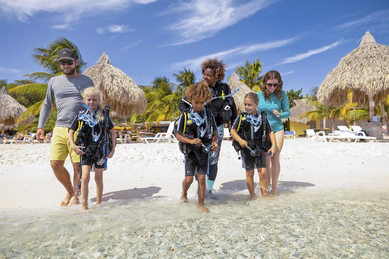 kids enetering water from beach in dive gear with adults