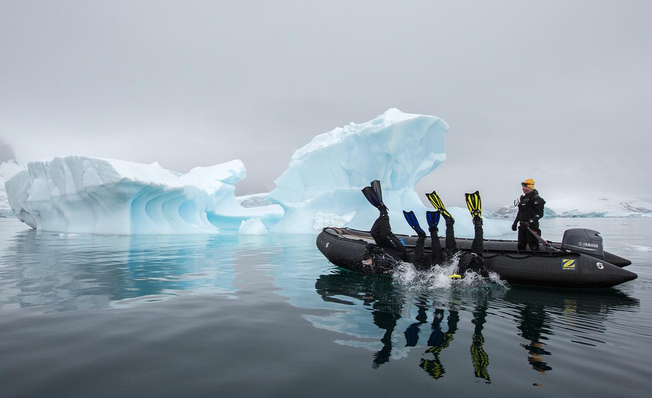 divers rolling into the water of antarctica off a zodiac