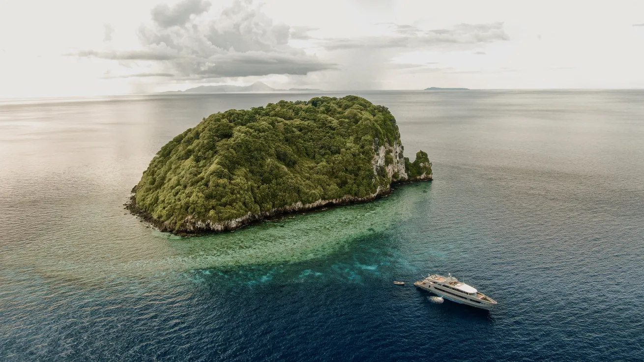 an aerial view of an island and a liveaboard in the foreground
