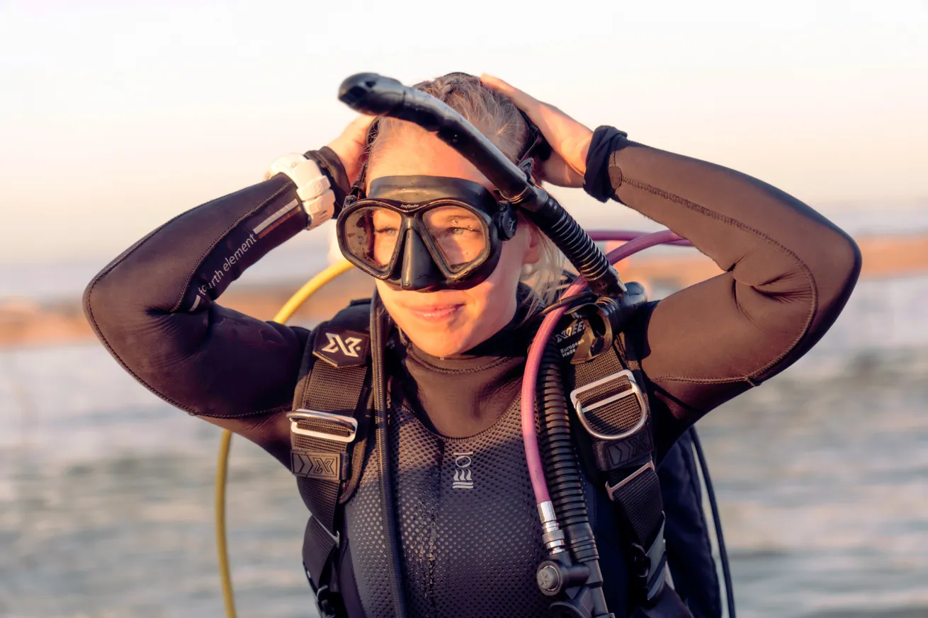 a woman putting scuba gear on at the beach