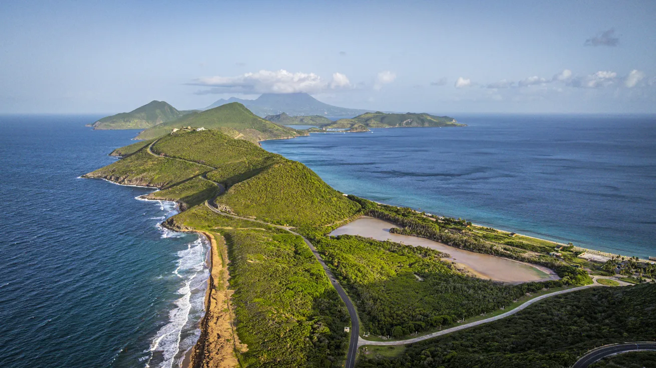 A panoramic view from Timothy Hill Overlook in Frigate Bay, where the Atlantic Ocean meets the Caribbean Sea, with the distant silhouette of Nevis gracing the horizon.

